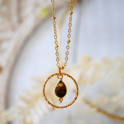 Nahaufnahme einer filigranen Edelstahlkette mit rundem Tigerauge-Anhänger, der goldbraun schimmert. Die Kette liegt auf weißem Hintergrund.