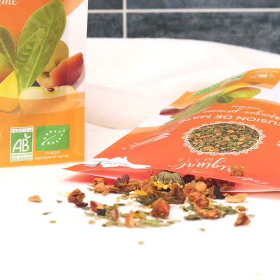 Offene Packung Bio-Mate Apfel Mango mit sichtbaren Mangostücken, Apfel und Ringelblumenblüten.
