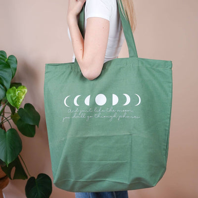 Grüne Baumwolltasche mit Mondphasen-Print und dem Spruch „And just like the moon, you shall go through phases“, getragen über der Schulter.