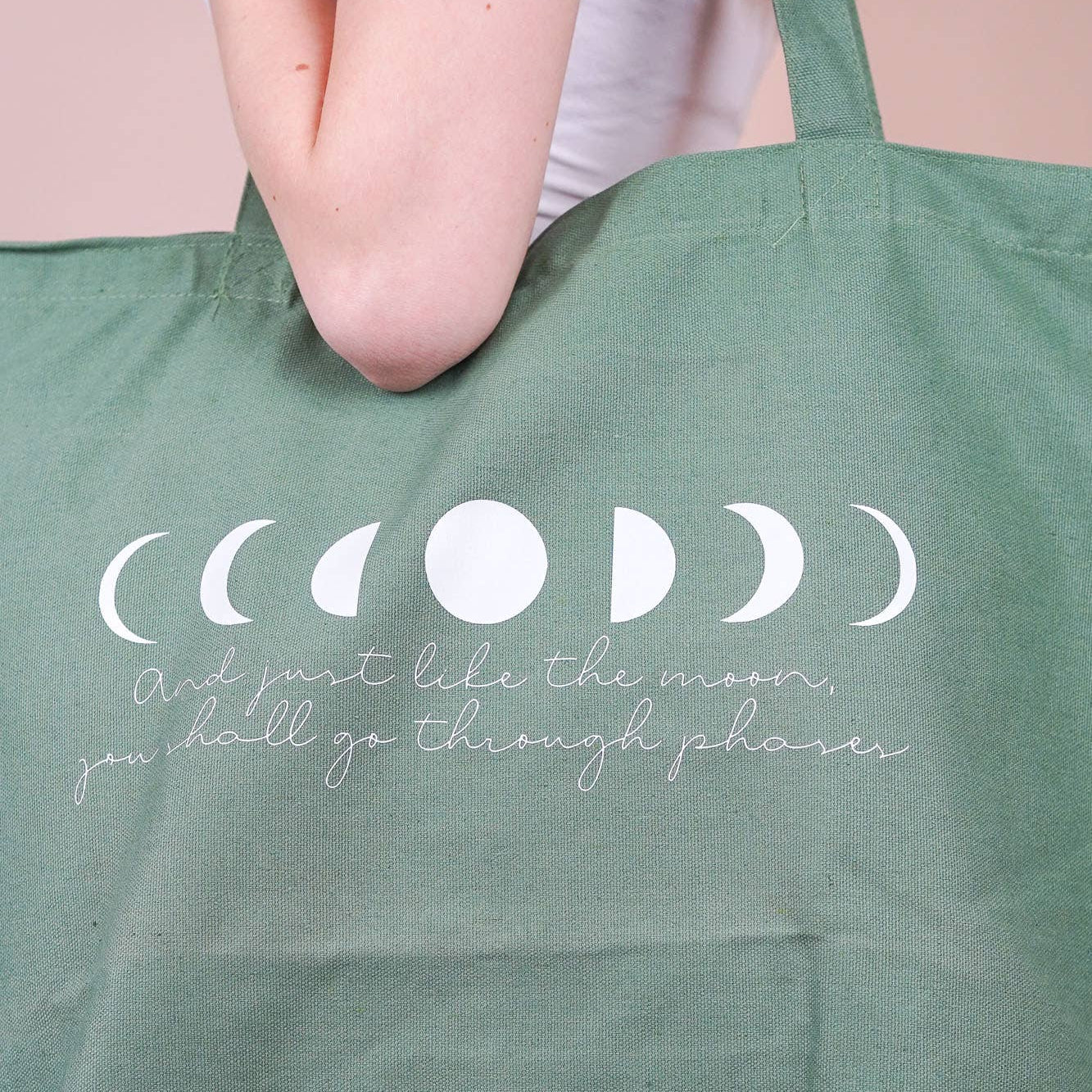 Grüne Hellblaue Baumwolltasche mit Mondphasen-Print und dem Spruch „And just like the moon, you shall go through phases“, getragen über der Schulter großformatig