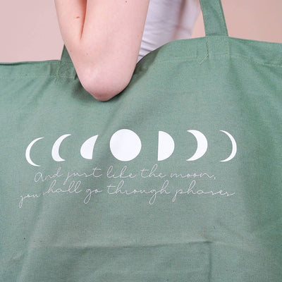 Grüne Hellblaue Baumwolltasche mit Mondphasen-Print und dem Spruch „And just like the moon, you shall go through phases“, getragen über der Schulter großformatig