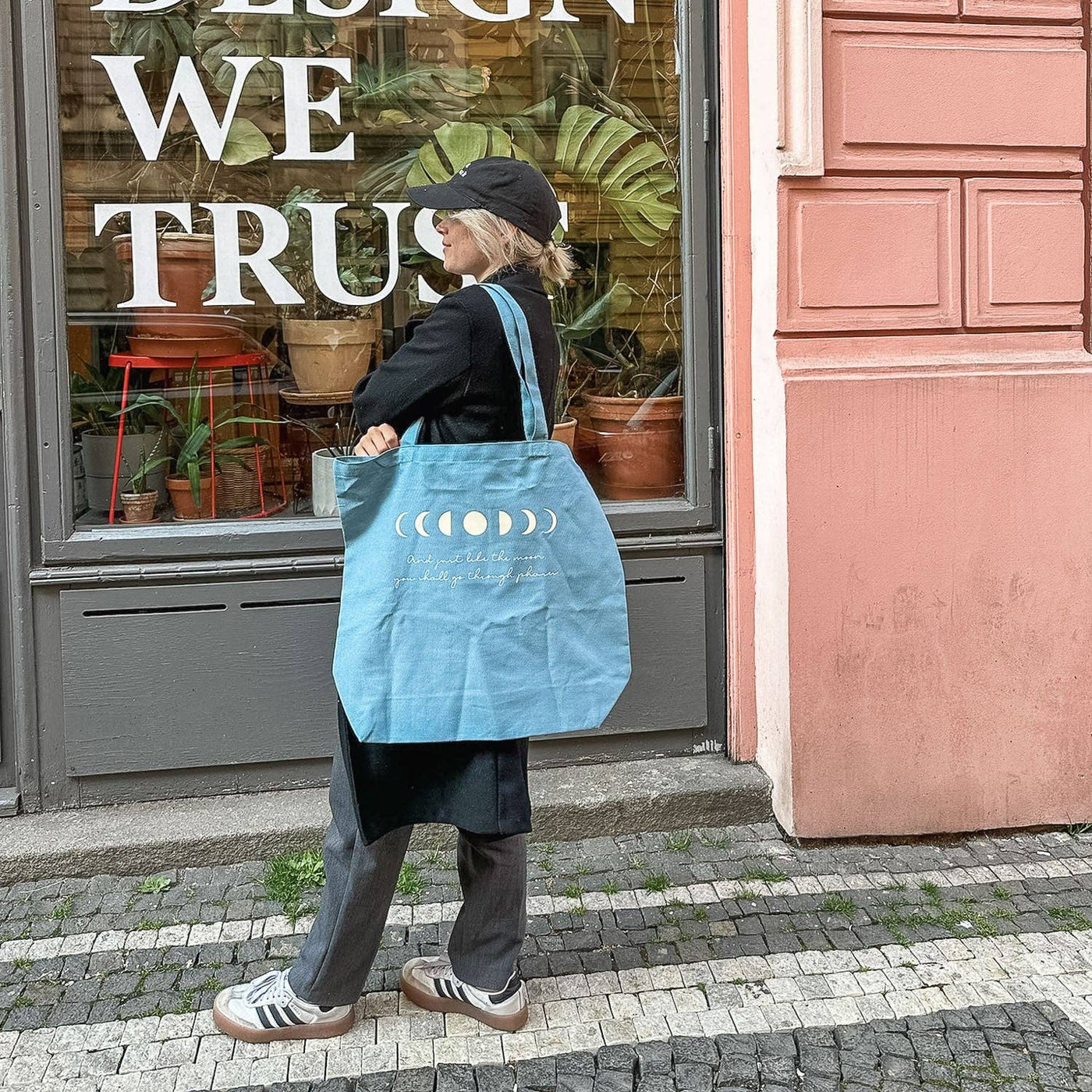 Hellblaue Baumwolltasche mit Mondphasen-Print und dem Spruch „And just like the moon, you shall go through phases“, getragen über der Schulter.