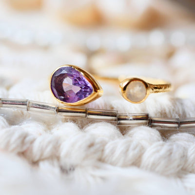 Verstellbarer Goldring mit gehämmertem Effekt, besetzt mit Amethyst und Regenbogen-Mondstein, auf hellem Hintergrund.