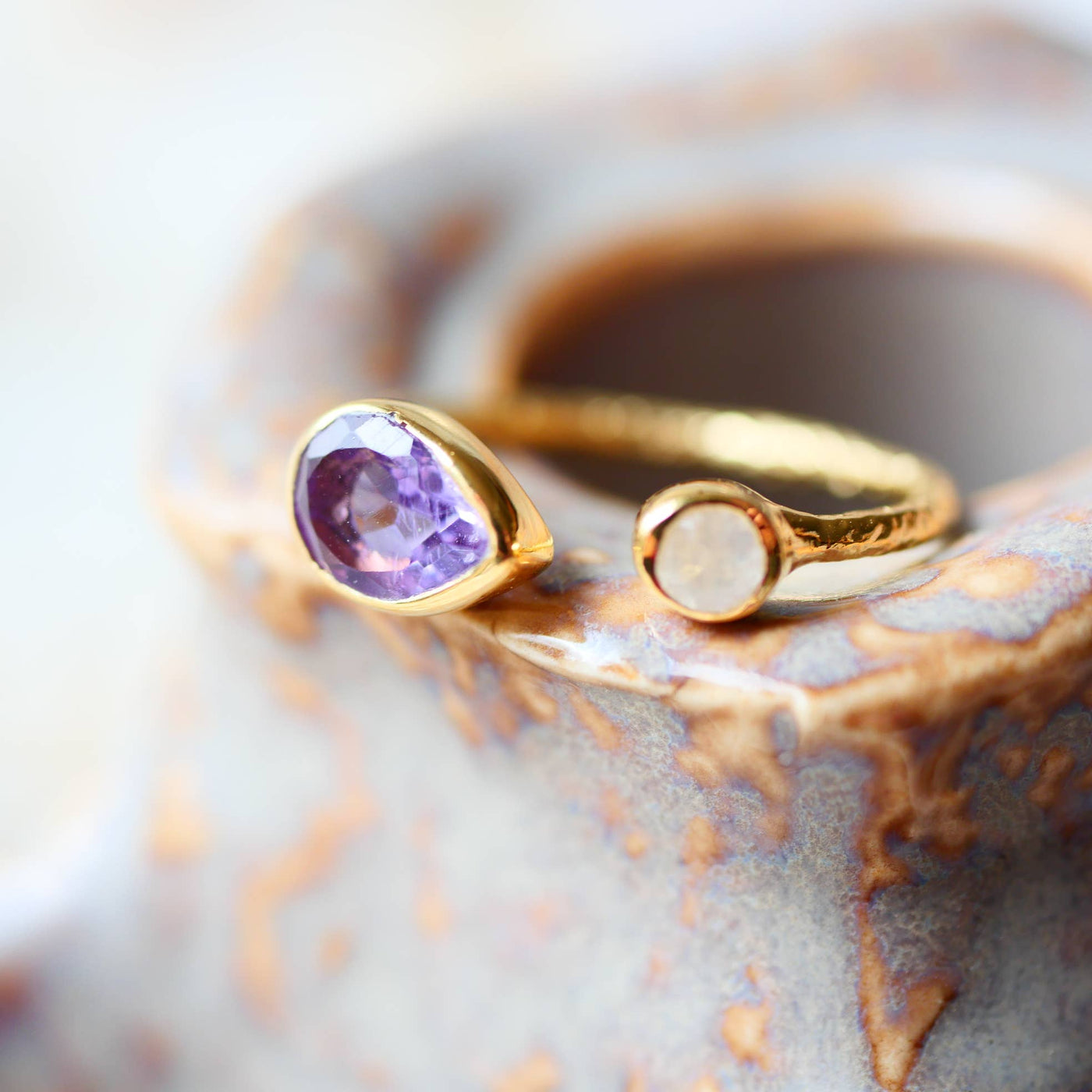 Verstellbarer Goldring mit gehämmertem Effekt, besetzt mit Amethyst und Regenbogen-Mondstein, auf hellem Hintergrund.