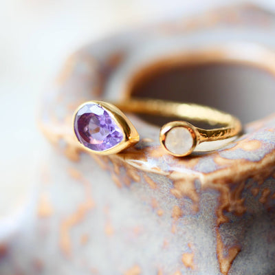 Verstellbarer Goldring mit gehämmertem Effekt, besetzt mit Amethyst und Regenbogen-Mondstein, auf hellem Hintergrund.