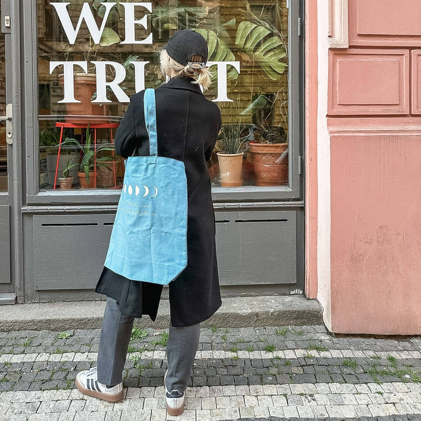 Hellblaue Baumwolltasche mit Mondphasen-Print und dem Spruch „And just like the moon, you shall go through phases“, getragen über der Schulter.