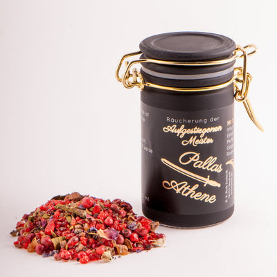Ein kleines Glas mit ca. 60 ml Räuchermischung „Pallas Athene – Aufgestiegene Meister“ von Berk; im Vordergrund liegen einige der Zutaten wie Myrrhe, rote Pfefferkörner und Pflanzenstücke, im Hintergrund stimmungsvolles, warmes Licht, das eine Aura von Mystik und Weisheit entstehen lässt.