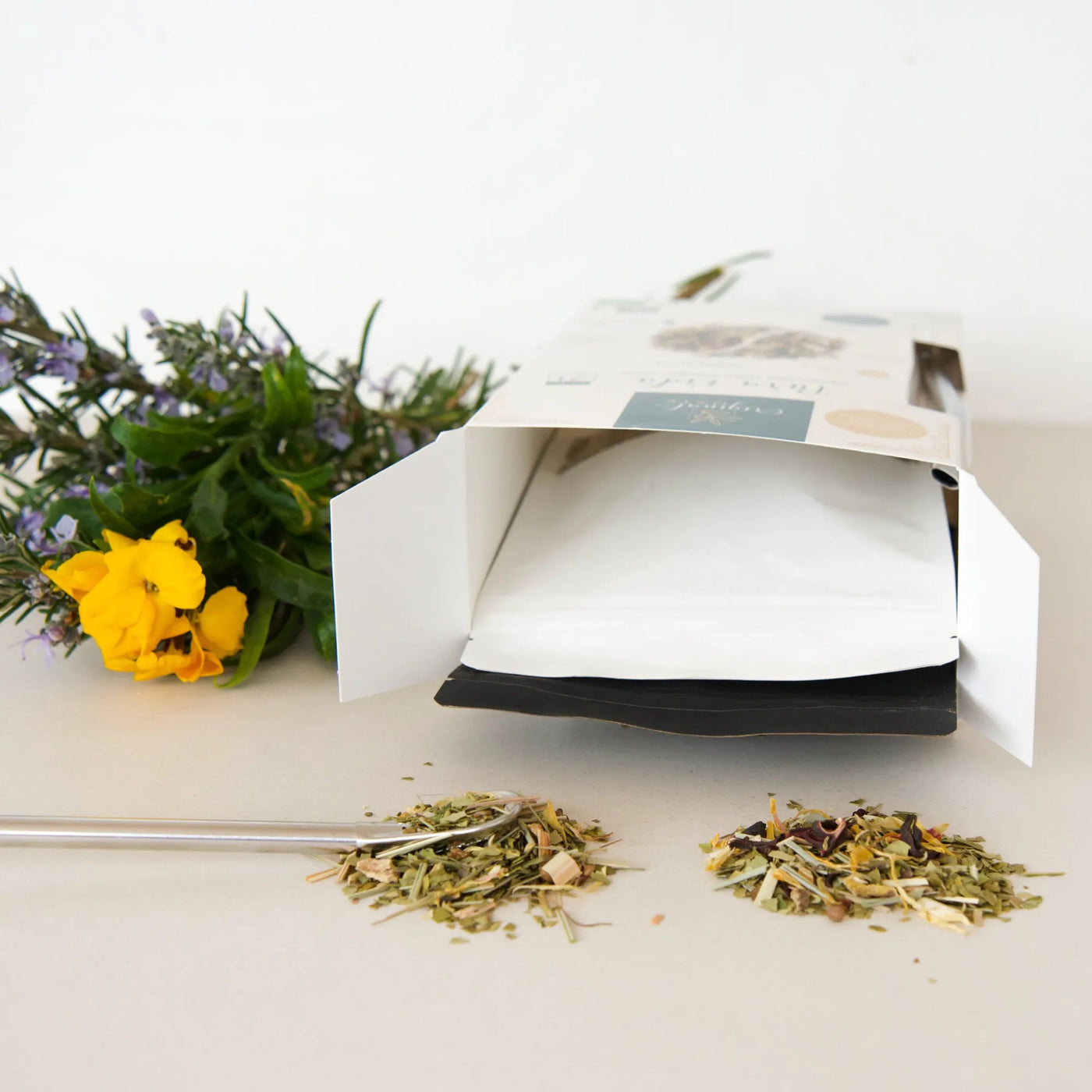 „Mate-Teemischung Pura Vida Día und Noche, ausgegossen vor der geöffneten Verpackung, mit floraler Dekoration.“ - Dianas Klosterlädchen